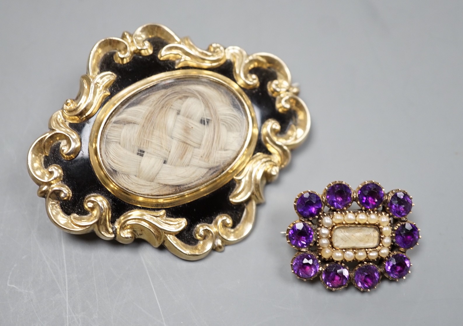 Two Victorian yellow metal (tests as 9ct) mourning brooches, one with black enamel and pendant bale, 51mm, the other with amethyst and seed pearl, both with plaited hair beneath a glazed panel.